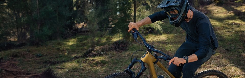 Mountainbiker mit Vollvisierhelm fährt auf Trail durch den Wald, am Handgelenk eine Garmin Sportuhr