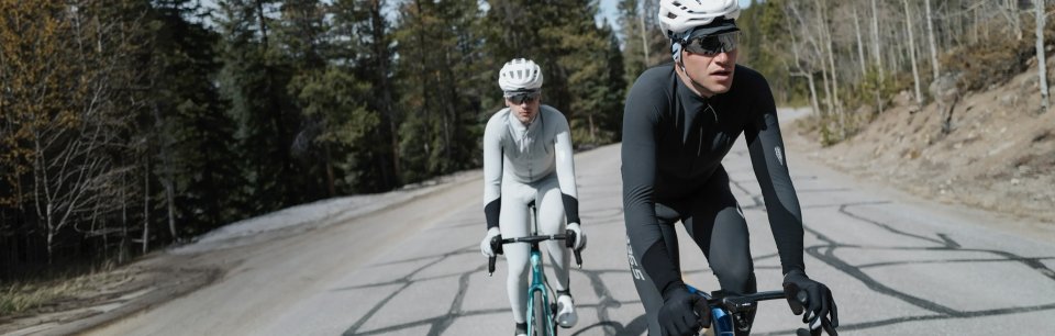 Zwei Radfahrer erklimmen in Q36.5 Kit eine schneebedeckte Bergstraße durch den Wald