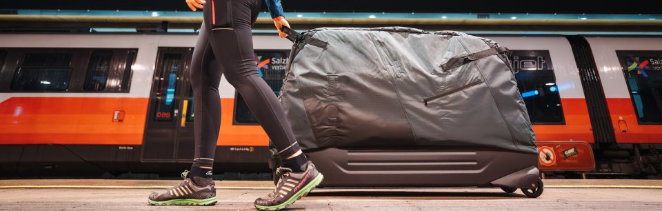 Iemand trekt een B&W International fietskoffer over het perron en laat zien hoe je je fiets veilig en makkelijk mee kunt nemen op reis.