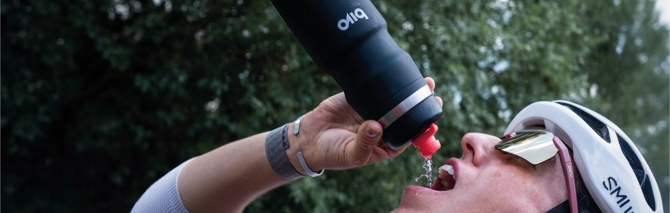 Een fietser houdt zijn hoofd achterover en drinkt uit een zwarte Bivo-bidon.