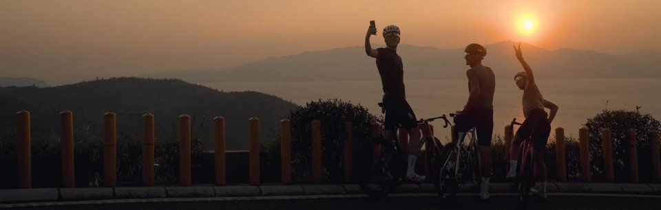 Drei Rennradfahrer machen bei Sonnenuntergang mit ihren Rädern Pause am Meer, unterwegs mit iGPSPORT