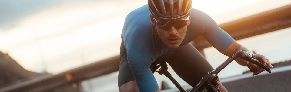 Rennradfahrer in tiefer, aerodynamischer Haltung im Abendlicht, im blauen PISSEI Radtrikot