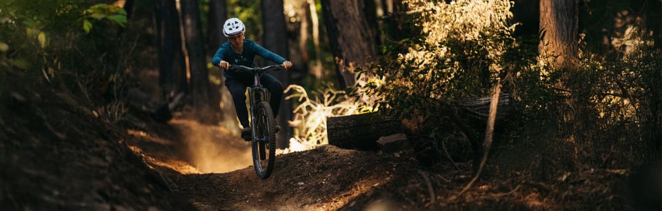 Une femme portant un casque FOX Racing roule sur un chemin forestier.