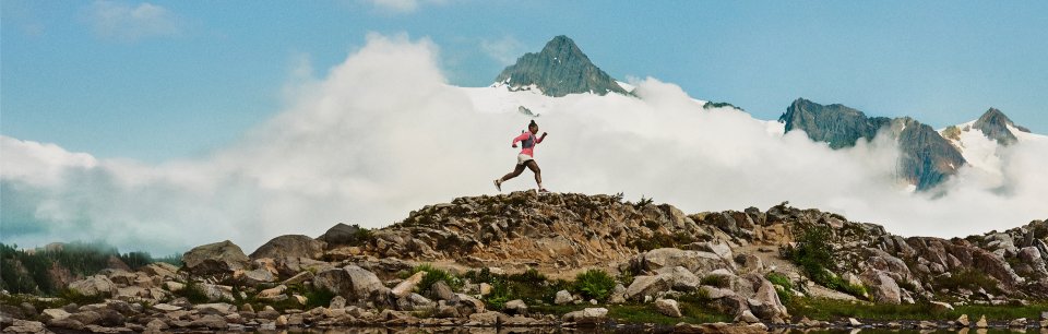 Trail tekač v čevljih HOKA prečka kamnit teren z ledenikom v ozadju.
