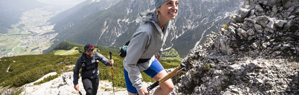 Deux coureurs de trail en vêtements outdoor VAUDE escaladent un sommet pierreux sous le soleil.