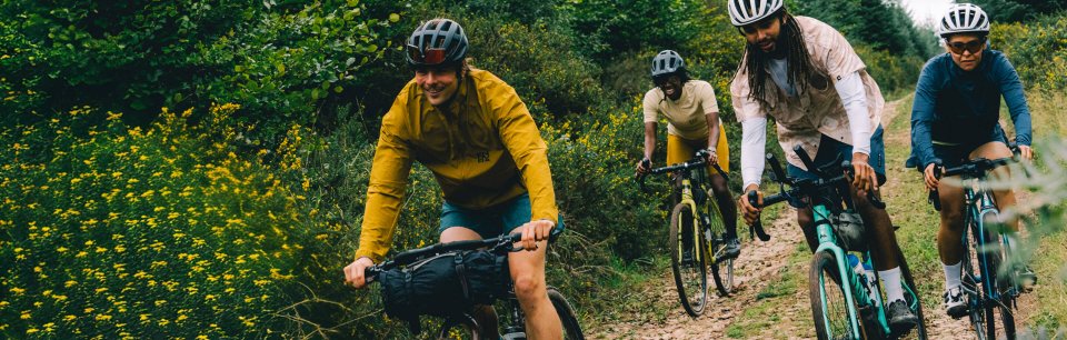 Drie fietsers in Endura-fietskleding rijden bij zonsondergang op een pad langs de kust.