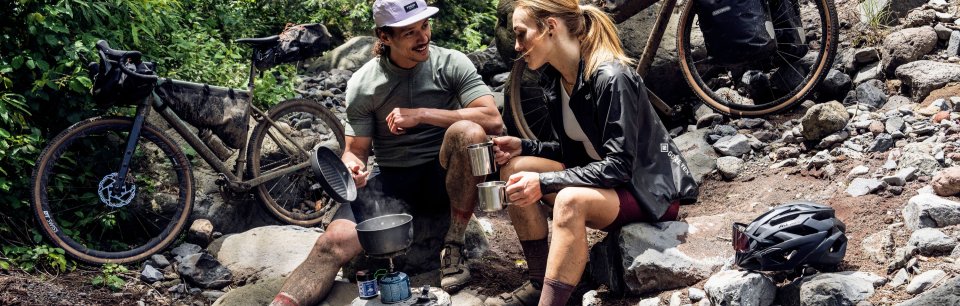 Deux cyclotouristes prennent un repas à côté de vélos remplis de sacoches ORTLIEB.