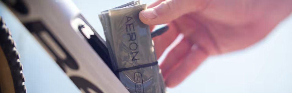 Une main range une chambre à air de vélo en TPU pliée portant l'inscription « AERON » dans le cadre d'un vélo.