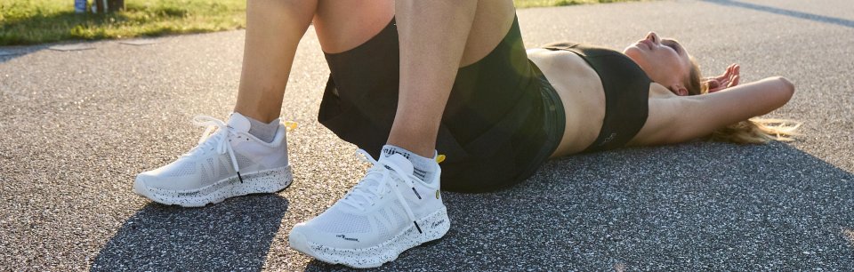 Sportliche Frau erholt sich nach dem Lauf, trägt weiße Joe Nimble Laufschuhe.