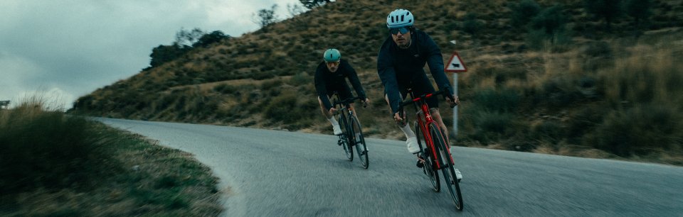 Dos personas ciclistas en una carretera en un dia nublado con cascos de la marca Sweet Protection
