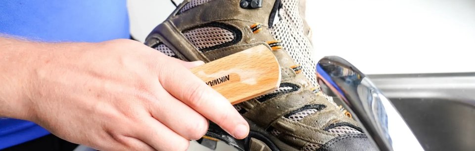 Persona limpiando el calzado de montaña con un cepillo y producto de la marca Nikwax