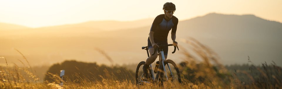 Wielrenner op een Cube-racefiets bij zonsondergang in een heuvelachtig landschap.