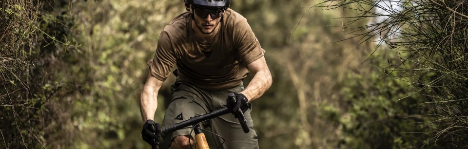 Hombre sobre una bicicleta en el bosque con ropa de color verde, gafas y casco de ciclismo